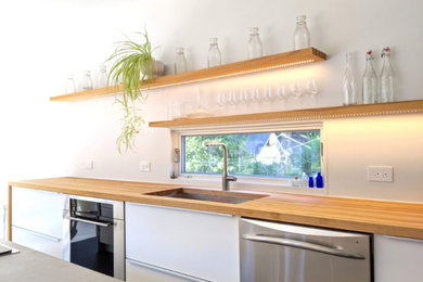 Example of a large trendy galley porcelain tile and black floor eat-in kitchen design in New York with an undermount sink, flat-panel cabinets, white cabinets, concrete countertops, white backsplash, window backsplash, stainless steel appliances, an island and gray countertops