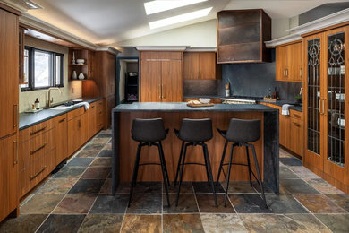 Eat-in kitchen - large eclectic l-shaped slate floor, multicolored floor and vaulted ceiling eat-in kitchen idea in Detroit with an undermount sink, flat-panel cabinets, medium tone wood cabinets, soapstone countertops, black backsplash, stone slab backsplash, paneled appliances, an island and black countertops