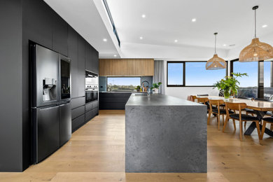 Design ideas for an expansive contemporary kitchen pantry in Geelong with a double-bowl sink, flat-panel cabinets, black cabinets, engineered stone countertops, grey splashback, engineered quartz splashback, black appliances, light hardwood flooring, an island and grey worktops.