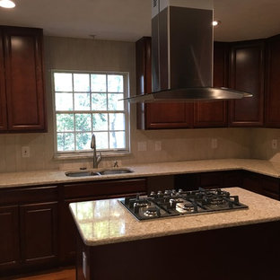 This is an example of a large traditional u-shaped kitchen pantry in DC Metro with an undermount sink, raised-panel cabinets, brown cabinets, granite benchtops, beige splashback, cement tile splashback, black appliances, light hardwood floors and with island.