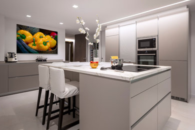 Large contemporary u-shaped open plan kitchen in Barcelona with a double-bowl sink, flat-panel cabinets, beige cabinets, stainless steel appliances, ceramic floors, with island and beige floor.