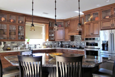 Example of a mid-sized classic l-shaped medium tone wood floor and brown floor eat-in kitchen design in Other with a drop-in sink, raised-panel cabinets, medium tone wood cabinets, quartzite countertops, gray backsplash, stone tile backsplash, stainless steel appliances, an island and multicolored countertops