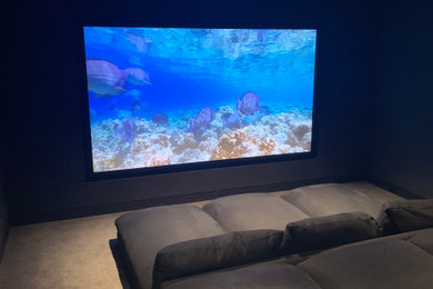 Medium sized modern enclosed home cinema in San Francisco with black walls, carpet, a projector screen and beige floors.