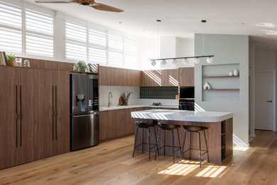 Design ideas for a mid-sized l-shaped kitchen in Melbourne with a double-bowl sink, medium wood cabinets, quartz benchtops, green splashback, mosaic tile splashback, black appliances, with island and white benchtop.