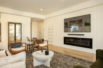 Foto de sala de estar machihembrado y abierta ecléctica de tamaño medio con paredes blancas, suelo laminado, pared multimedia y suelo marrón