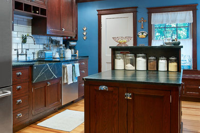 Inspiration for a mid-sized country l-shaped light wood floor enclosed kitchen remodel in Providence with a farmhouse sink, recessed-panel cabinets, dark wood cabinets, soapstone countertops, white backsplash, subway tile backsplash, stainless steel appliances and an island