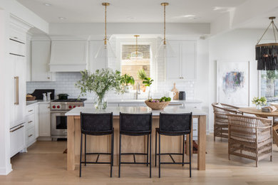 Inspiration for a mid-sized beach style l-shaped eat-in kitchen in Minneapolis with an undermount sink, shaker cabinets, white cabinets, quartz benchtops, white splashback, subway tile splashback, stainless steel appliances, light hardwood floors, with island, brown floor and white benchtop.