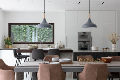Inspiration for a large modern galley open plan kitchen in Gloucestershire with a submerged sink, flat-panel cabinets, white cabinets, quartz worktops, beige splashback, stainless steel appliances, concrete flooring, an island, white floors and beige worktops.