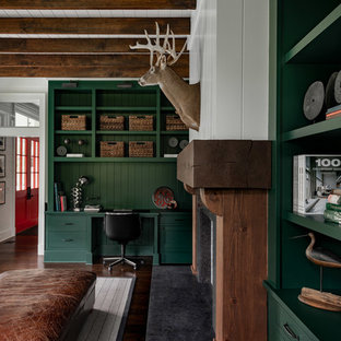 Photo of a large country home office in New York with a library, white walls, dark hardwood floors, a standard fireplace, a wood fireplace surround, a built-in desk and brown floor.
