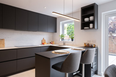 Inspiration for a contemporary u-shaped gray floor kitchen remodel in Gloucestershire with an undermount sink, flat-panel cabinets, black cabinets, white backsplash, stone slab backsplash, paneled appliances, a peninsula and white countertops