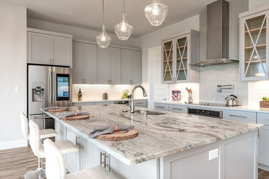 Mid-sized transitional l-shaped open plan kitchen in Austin with a double-bowl sink, shaker cabinets, grey cabinets, granite benchtops, white splashback, subway tile splashback, stainless steel appliances, medium hardwood floors, with island, brown floor and grey benchtop.