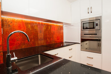 This is an example of a mid-sized eclectic u-shaped separate kitchen in Townsville with an undermount sink, white cabinets, quartz benchtops, red splashback, stainless steel appliances, ceramic floors and no island.