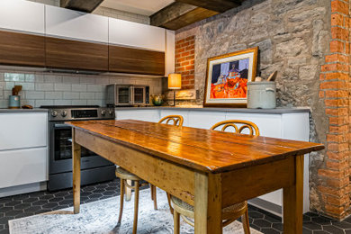 Inspiration for a mid-sized rustic u-shaped ceramic tile, black floor and exposed beam eat-in kitchen remodel in Toronto with a farmhouse sink, flat-panel cabinets, white cabinets, quartz countertops, white backsplash, subway tile backsplash, stainless steel appliances, an island and gray countertops