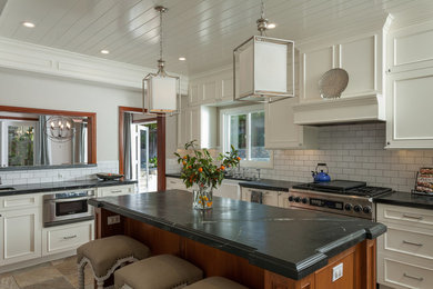 Beach style gray floor enclosed kitchen photo in Phoenix with a farmhouse sink, recessed-panel cabinets, white cabinets, white backsplash, subway tile backsplash, stainless steel appliances and an island