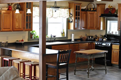 Example of a mid-sized classic u-shaped slate floor and gray floor open concept kitchen design in Burlington with a drop-in sink, raised-panel cabinets, medium tone wood cabinets, solid surface countertops, black backsplash, stone slab backsplash, black appliances and an island