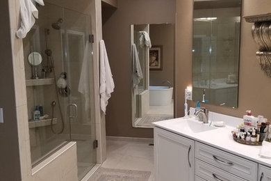 Photo of a large traditional master wet room bathroom in Cedar Rapids with beaded inset cabinets, white cabinets, a freestanding tub, a two-piece toilet, beige tile, porcelain tile, brown walls, porcelain floors, a console sink, engineered quartz benchtops, beige floor, a hinged shower door and white benchtops.
