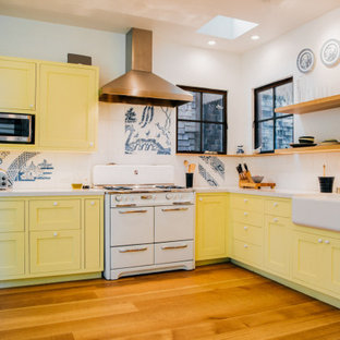 Exemple d'une grande arrière-cuisine éclectique en L avec un évier de ferme, un placard à porte shaker, des portes de placard jaunes, une crédence blanche, une crédence en carreau de porcelaine, un électroménager blanc, un sol en bois brun, aucun îlot, un sol marron et un plan de travail blanc.