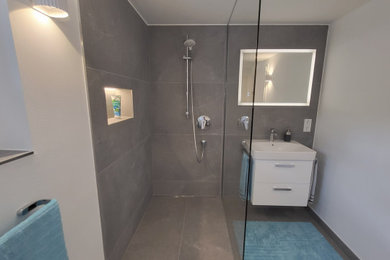 Mittelgroßes Modernes Duschbad mit flächenbündigen Schrankfronten, weißen Schränken, bodengleicher Dusche, Wandtoilette, grauen Fliesen, Zementfliesen, weißer Wandfarbe, Porzellan-Bodenfliesen, Unterbauwaschbecken, Mineralwerkstoff-Waschtisch, grauem Boden, offener Dusche, weißer Waschtischplatte, Einzelwaschbecken und schwebendem Waschtisch in Frankfurt am Main