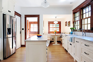 Mid-sized arts and crafts galley eat-in kitchen in Indianapolis with with island, a farmhouse sink, beaded inset cabinets, white cabinets, quartz benchtops, white splashback, ceramic splashback, stainless steel appliances, medium hardwood floors, brown floor and grey benchtop.
