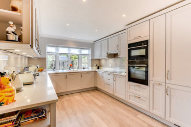 This is an example of a medium sized classic grey and white u-shaped enclosed kitchen in Sussex with a submerged sink, shaker cabinets, grey cabinets, quartz worktops, beige splashback, glass sheet splashback, black appliances, vinyl flooring, no island, brown floors, white worktops and feature lighting.