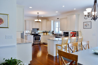 Mid-sized arts and crafts galley eat-in kitchen in DC Metro with a single-bowl sink, raised-panel cabinets, white cabinets, granite benchtops, glass sheet splashback, stainless steel appliances, medium hardwood floors, metallic splashback, a peninsula and brown floor.