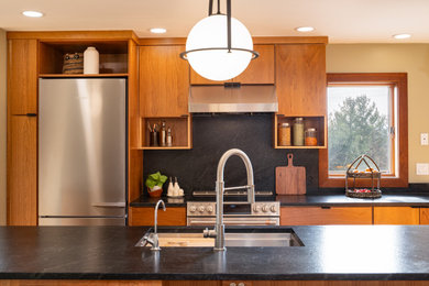 Kitchen - large contemporary galley light wood floor kitchen idea in Other with a single-bowl sink, flat-panel cabinets, granite countertops, black backsplash, granite backsplash, stainless steel appliances, an island and black countertops