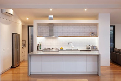 Small contemporary l-shaped open plan kitchen in Melbourne with a double-bowl sink, flat-panel cabinets, white cabinets, granite benchtops, white splashback, subway tile splashback, stainless steel appliances, medium hardwood floors and with island.