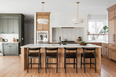 Inspiration for a large transitional l-shaped light wood floor and brown floor open concept kitchen remodel with an undermount sink, shaker cabinets, light wood cabinets, solid surface countertops, white backsplash, matchstick tile backsplash, paneled appliances, an island and white countertops