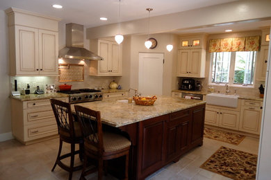 Inspiration for a large timeless u-shaped travertine floor eat-in kitchen remodel in Los Angeles with a farmhouse sink, raised-panel cabinets, white cabinets, granite countertops, beige backsplash, stone tile backsplash, stainless steel appliances and an island