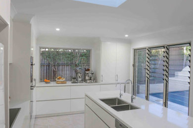 Photo of a mid-sized beach style galley kitchen in Brisbane with with island and white benchtop.