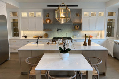 Inspiration for a large country l-shaped light wood floor, brown floor, exposed beam and shiplap ceiling open concept kitchen remodel in Los Angeles with glass-front cabinets, white backsplash, ceramic backsplash, stainless steel appliances, an island, white countertops, a farmhouse sink, white cabinets and quartzite countertops