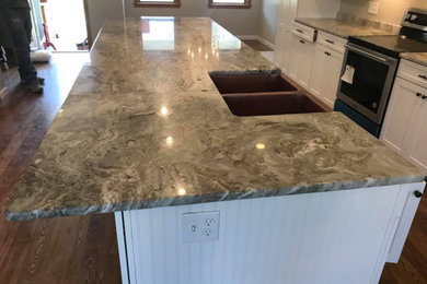 Example of a large galley kitchen design in Boston with a farmhouse sink, shaker cabinets, white cabinets, granite countertops, gray backsplash, granite backsplash, stainless steel appliances, an island and gray countertops