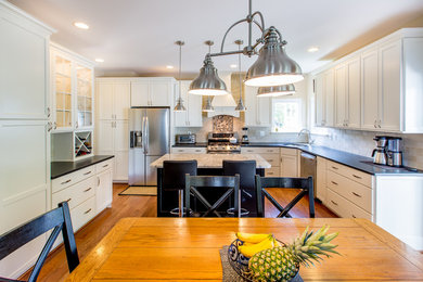 Large traditional l-shaped eat-in kitchen in DC Metro with an undermount sink, glass-front cabinets, white cabinets, granite benchtops, multi-coloured splashback, subway tile splashback, stainless steel appliances, medium hardwood floors and with island.