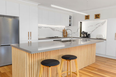 Design ideas for a large beach style l-shaped eat-in kitchen in Melbourne with an undermount sink, flat-panel cabinets, white cabinets, quartz benchtops, multi-coloured splashback, porcelain splashback, black appliances, medium hardwood floors, with island and grey benchtop.