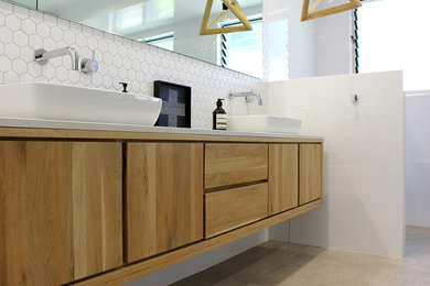 This is an example of a large modern ensuite bathroom in Sydney with glass-front cabinets, light wood cabinets, a shower/bath combination, white tiles, porcelain tiles, white walls, porcelain flooring, a console sink and granite worktops.