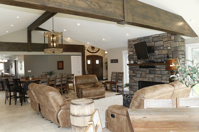 Example of a large mountain style open concept beige floor living room design in Other with beige walls, a standard fireplace, a stone fireplace and a wall-mounted tv