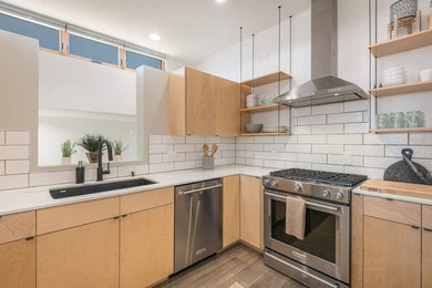 Open concept kitchen - mid-sized modern l-shaped medium tone wood floor and brown floor open concept kitchen idea in Albuquerque with an undermount sink, flat-panel cabinets, light wood cabinets, marble countertops, white backsplash, subway tile backsplash, stainless steel appliances, a peninsula and white countertops