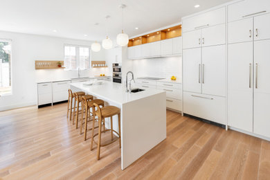Design ideas for a mid-sized scandinavian l-shaped eat-in kitchen in Ottawa with an undermount sink, flat-panel cabinets, white cabinets, quartz benchtops, white splashback, porcelain splashback, panelled appliances, light hardwood floors, with island and white benchtop.
