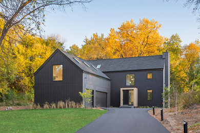 Réalisation d'une grande façade de maison noire nordique en bois et planches et couvre-joints à un étage avec un toit à deux pans, un toit en shingle et un toit noir.