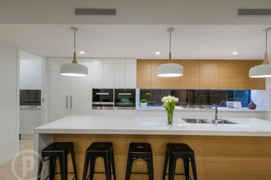 This is an example of a large contemporary galley eat-in kitchen in Brisbane with an undermount sink, medium wood cabinets, quartz benchtops, metallic splashback, glass sheet splashback, stainless steel appliances, light hardwood floors and with island.