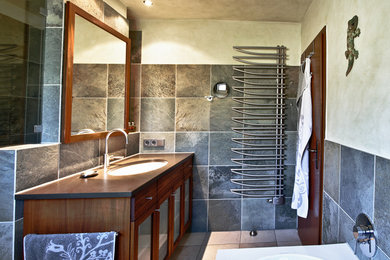 Kleines Landhaus Badezimmer En Suite mit Mineralwerkstoff-Waschtisch, Glasfronten, dunklen Holzschränken, Einbaubadewanne, grauen Fliesen, Schieferfliesen, grauer Wandfarbe, Einbauwaschbecken, beigem Boden und brauner Waschtischplatte in Köln