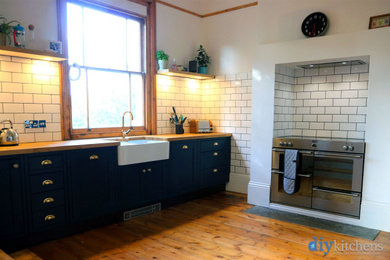 На фото: п-образная кухня среднего размера в классическом стиле с обеденным столом, фасадами в стиле шейкер, синими фасадами, деревянной столешницей и коричневой столешницей без острова