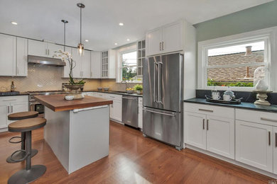 Inspiration for a mid-sized transitional l-shaped medium tone wood floor and brown floor eat-in kitchen remodel in San Francisco with an undermount sink, shaker cabinets, white cabinets, soapstone countertops, beige backsplash, ceramic backsplash, stainless steel appliances, an island and black countertops