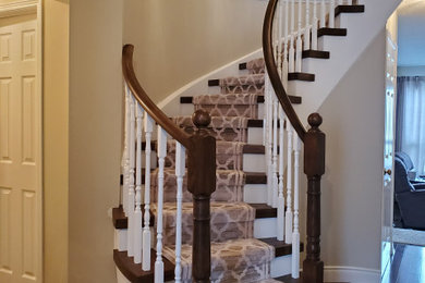 Large trendy wooden curved staircase photo in Toronto with painted risers