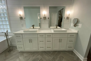 Large minimalist master white tile and subway tile wood-look tile floor, gray floor, double-sink, tray ceiling and shiplap wall bathroom photo in Jacksonville with shaker cabinets, white cabinets, a one-piece toilet, gray walls, a vessel sink, granite countertops, a hinged shower door, white countertops, a niche and a freestanding vanity