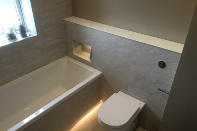 Medium sized modern family bathroom in Other with freestanding cabinets, light wood cabinets, a built-in bath, a shower/bath combination, a one-piece toilet, grey tiles, porcelain tiles, grey walls, porcelain flooring and a wall-mounted sink.