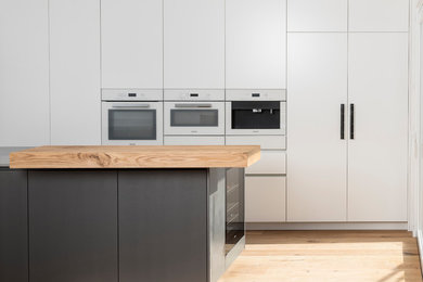 Küche mit flächenbündigen Schrankfronten, weißen Schränken, Quarzwerkstein-Arbeitsplatte, Küchenrückwand in Weiß, Glasrückwand, braunem Holzboden, Kücheninsel, braunem Boden und grauer Arbeitsplatte in Sonstige