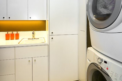 Example of a minimalist laundry room design in San Francisco with a stacked washer/dryer and white cabinets