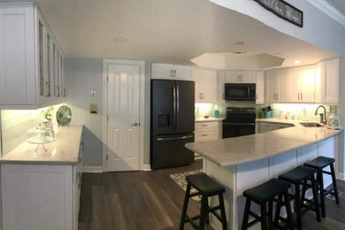 Example of a mid-sized transitional u-shaped dark wood floor, brown floor and tray ceiling kitchen pantry design in Other with an undermount sink, recessed-panel cabinets, white cabinets, granite countertops, green backsplash, ceramic backsplash, black appliances, a peninsula and gray countertops