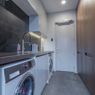 This is an example of a large modern galley separated utility room in Auckland with an integrated sink, flat-panel cabinets, dark wood cabinets, stainless steel worktops, grey walls, concrete flooring, a side by side washer and dryer and grey floors.